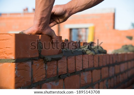 Bricklayer worker installing brick masonry on exterior wall. Professional construction worker laying bricks. Royalty-Free Stock Photo #1895143708