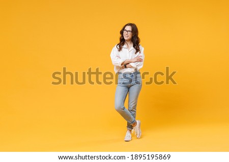 Smiling young brunette business woman in white shirt glasses isolated on yellow background studio. Achievement career wealth business concept. Mock up copy space. Holding hands crossed, looking aside Royalty-Free Stock Photo #1895195869