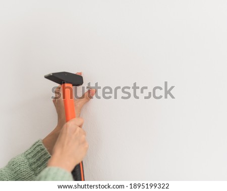 close up picture of a woman nailing a hammer on the wall