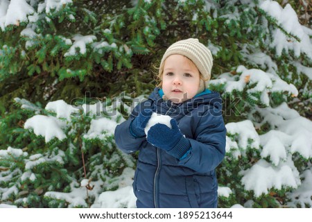 Happy child having fun in the snow outdoor in winter day. Cute little toddler with warm clothes playing in park or backyard, winter activities for kids