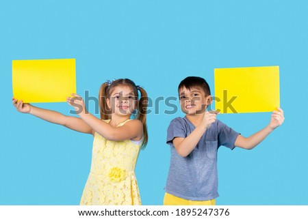 Preschool kids posing with yellow letterhead for your advertisement. Photo on a blue background.