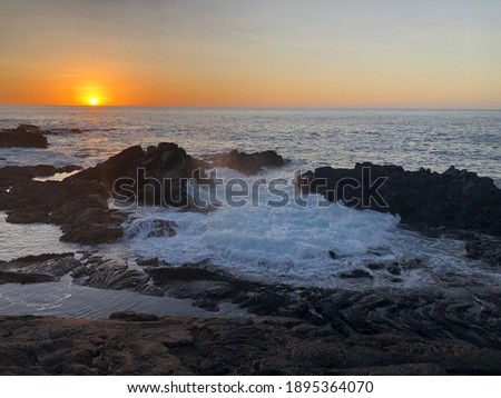 Sunset dipping below the horizon over waves rolling onto the lava rock shore. 