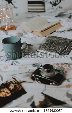 A vertical shot of an open book, mug, notebook, and a retro photo camera on the bedspread, the concept hobby and leisure time