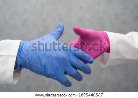 Two people from the healthcare industry shake hands from two different labs as a sign of working together and continuing to work together on the COVID19 vaccine together. Gray blurry background. Close