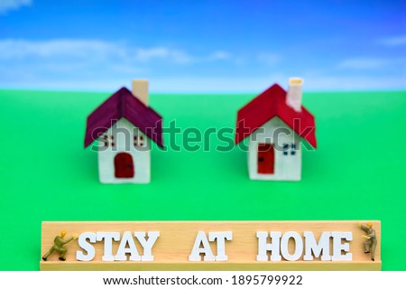 The words of Stay at home on wooden block on green background with blurred home against blue sky using for protect pandemic virus and quarantine for safety concept .