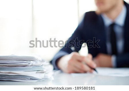Stack of documents at workplace and male employee on background Royalty-Free Stock Photo #189580181