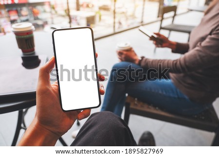 Mockup image of a hand holding mobile phone with blank white desktop screen with a woman using phone in background