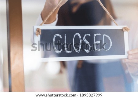 A waitress wearing protective face mask hanging closed sign on front door due to coronavirus pandemic effect