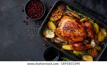 Roasted chicken in pomegranate sauce with potatoes in a gray ceramic mold. Dark background. Top view. Copy space Royalty-Free Stock Photo #1895855344