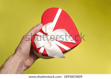Gift box in male hand on the yellow background. White ribbon. Valentines Day gift