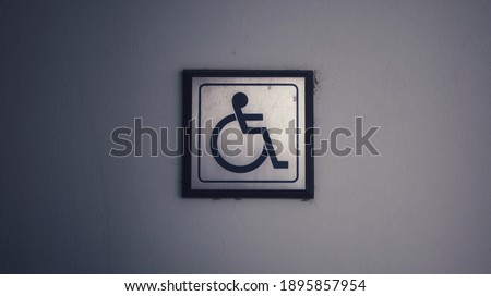 Close-up of a bronze wheelchair and a handicapped entrance sign on a cement wall.