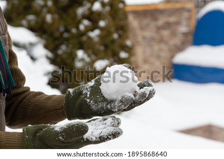Winter fun. Hands in green fleece gloves form snowballs on a frosty day close-up

