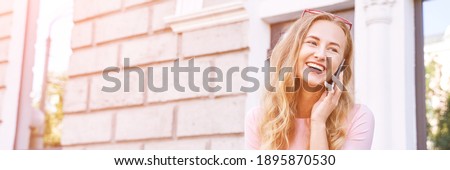 Pretty young woman talking by phone. Happy female person outdoors. Summer business portrait. Lady calling friends or boyfriend. Blonde long hair. Cute adult student at town