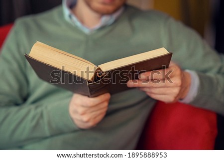 A man in a green sweater reading a book