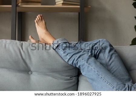 Crop close up of woman lying relaxing on comfortable grey couch in living room on lazy domestic weekend. Female renter or tenant rest barefoot on cozy sofa at home. Relaxation, pedicure concept. Royalty-Free Stock Photo #1896027925