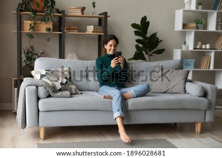 Smiling young Caucasian woman sit relax on couch in living room talk on video call. Happy millennial female rest on sofa at home have webcam digital virtual communication on cellphone. Royalty-Free Stock Photo #1896028681