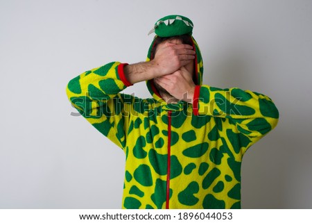 Young caucasian man wearing a pajama standing against white background Covering eyes and mouth with hands, surprised and shocked. Hiding emotions.