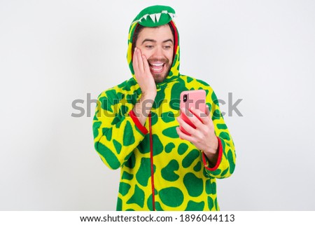 Young caucasian man wearing a pajama standing against white background holding in hands cell reading sms using new app 5g
