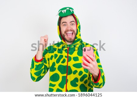 Portrait of Young caucasian man wearing a pajama standing against white background holding in hands cell celebrating
