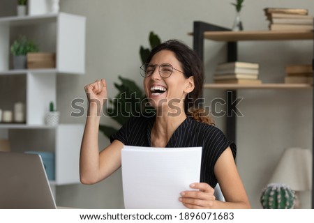 Overjoyed millennial Caucasian woman feel euphoric reading good news in post paper letter. Happy excited young female in glasses triumph receive amazing message in postal paperwork or correspondence. Royalty-Free Stock Photo #1896071683