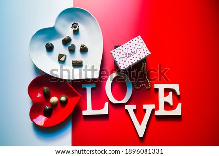 two heart-shaped dishes with chocolate bonbons on a red and white background and the word love