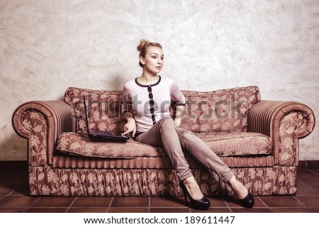 Technology internet modern lifestyle concept. Full length young business woman or student girl using laptop working on computer sitting on retro couch. Indoor. Vintage photo.