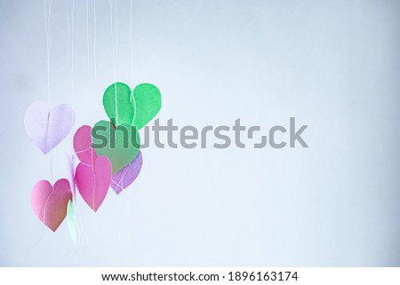 Paper blooming hearts sway from the wind on strings on a light background
