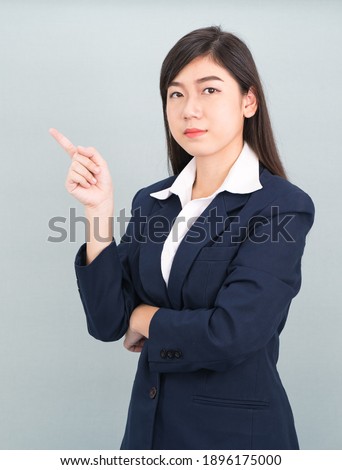 Asian businesswoman in suit with finger pointing up on gray background