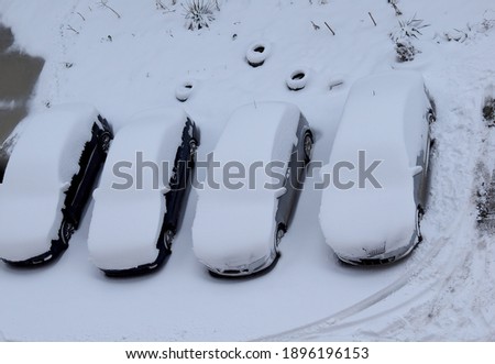 Four cars in the parking lot are covered with a thick layer of snow. A lot of snow fell on the street, everything around was covered with snow. The concept of weather anomaly, falling snow.