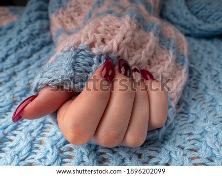 Stylish female manicure. Young female hand hold woolen material. nails with red manicure and white with hearts, on an blue wool background. Manicure at home during a pandemic