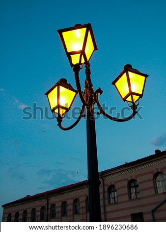 A lighted street lamp against the night sky. In the background, you can see a brick building. Close up, shooting from below. Street landscape. Evening atmospheric picture.
