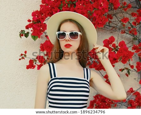 Portrait of beautiful woman wearing a summer straw hat on a red flowers background