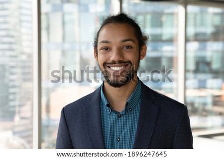 Headshot portrait of smiling young African American businessman in suit pose in own modern office. Profile picture of happy successful male boss or CEO in formalwear show confidence and leadership.