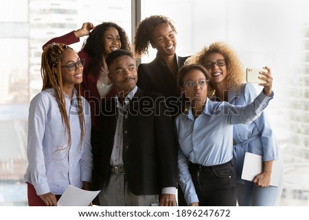Happy diverse multiethnic colleagues have fun make self-portrait picture on cellphone together. Smiling young multiracial businesspeople pose for selfie on smartphone in office. Technology concept.