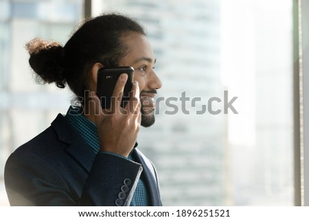 Smiling millennial African American businessman hold modern smartphone listen to audio message on loudspeaker. Happy male employee use digital voice assistant on cellphone. Technology concept.