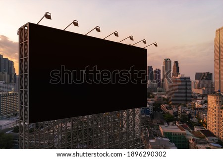 Blank black road billboard with Bangkok cityscape background at sunset. Street advertising poster, mock up, 3D rendering. Side view. The concept of marketing communication to promote or sell idea.