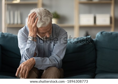 Frustrated unhappy middle aged mature man sitting on sofa, feeling depressed alone at home. Confused senior retired grandfather worrying about difficult life decision, copy space, old people solitude. Royalty-Free Stock Photo #1896308773