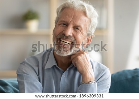 Head shot portrait of happy middle aged older retired man laughing at funny joke. Emotional smiling elderly grandfather looking at camera, enjoying video call or distant communicating with friends. Royalty-Free Stock Photo #1896309331