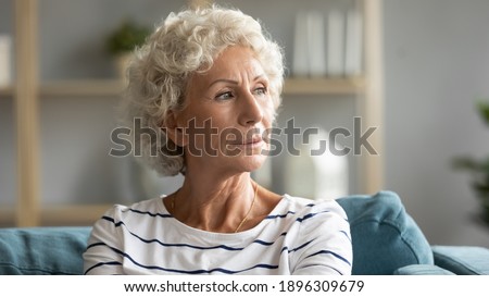 Head shot close up pensive old senior hoary woman looking in distance, recollecting memories or feeling lonely at home. Lost in thoughts middle aged grandmother relaxing on sofa, missing or mourning. Royalty-Free Stock Photo #1896309679