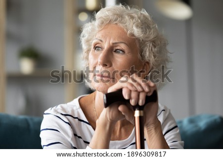 Head shot thoughtful elderly mature grandmother holding hands on walking wooden cane, looking in distance. Unhappy pensive disabled middle aged woman feeling lonely at home, recollecting memories. Royalty-Free Stock Photo #1896309817
