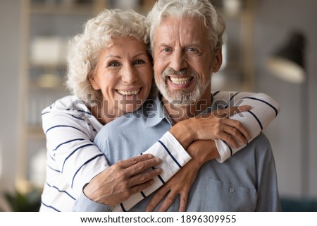 Head shot portrait of affectionate loving middle aged hoary beautiful woman cuddling from back smiling old husband. Happy loving mature married family couple looking at camera, posing for photo. Royalty-Free Stock Photo #1896309955