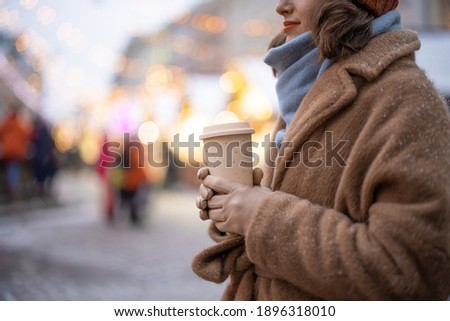 A woman holding takeaway coffee on the Christmas market background, walking in the downtown during holidays. High quality photo