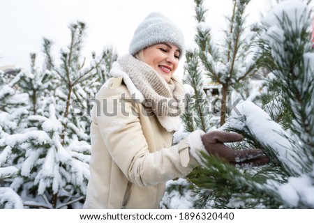 Beautiful woman standing among snowy trees in winter forest and enjoying first snow. Woman in winter woods.