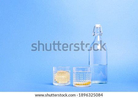 Glass with water and lemon near to bottle on blue background