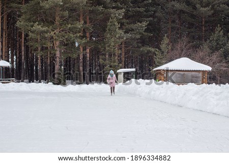 One girl in warm clothes rides on an ice rink near the forest. Winter sports recreation. Entertainment in quarantine