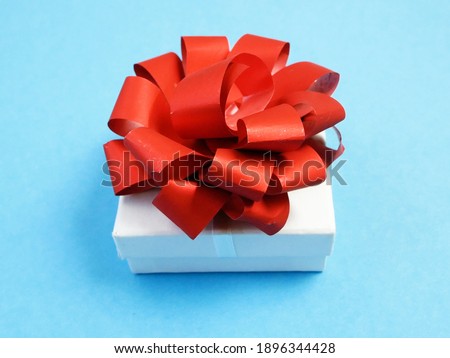 white gift box with red bow on blue background, top view, closeup