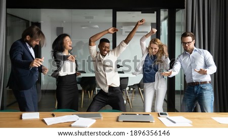 Crazy emotional young african american man having fun with happy diverse mixed race colleagues, dancing together in modern office, celebrating corporate success or profitable goal deal achievement. Royalty-Free Stock Photo #1896356146