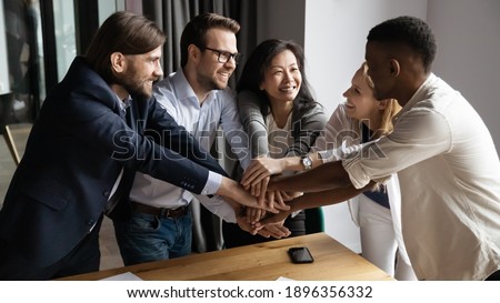 Excited happy young and mature mixed race colleagues joining hands, strengthening team spirit, motivating each other at meeting. Laughing diverse multiracial business people celebrating shared success Royalty-Free Stock Photo #1896356332