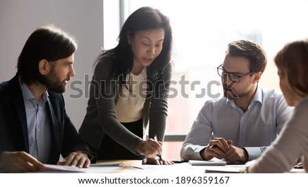 Serious middle aged older korean female team leader explaining company development strategy or sharing marketing research results to interested young diverse colleagues at briefing meeting in office. Royalty-Free Stock Photo #1896359167