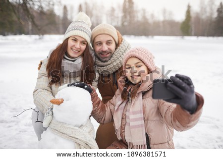 Portrait of happy family taking selfie photo outdoors while building snowman together and enjoying winter vacation, copy space